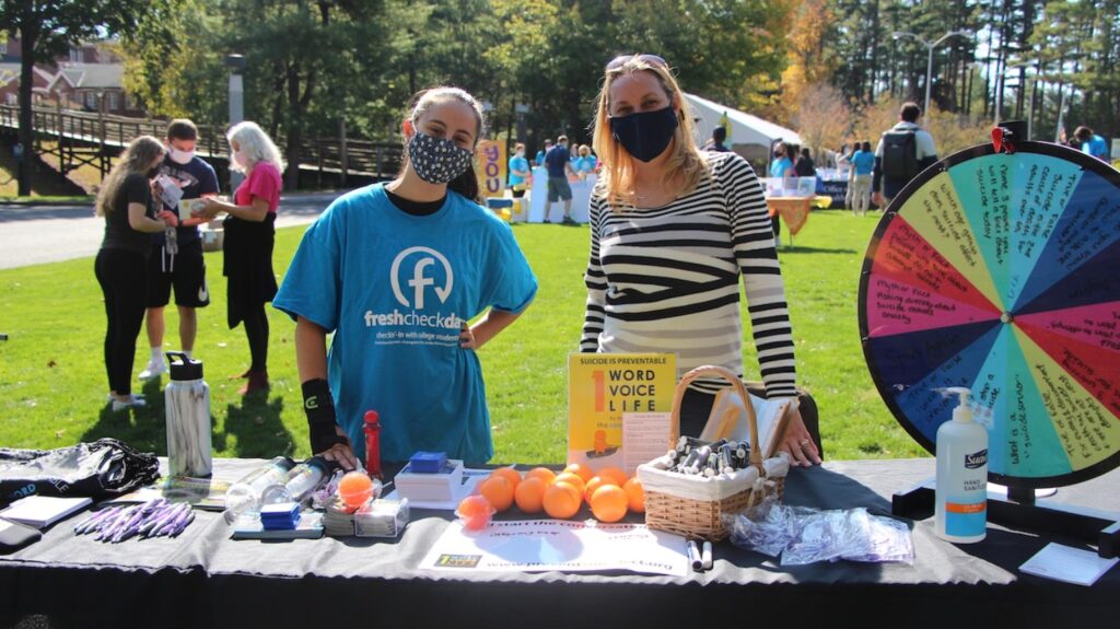 A faculty and student volunteer stand in front of the One Word, One Voice, One Life booth with the goal to promote suicide prevention by educating Connecticut residents and students. Asking the question can reduce the isolation a person in crisis feels and offers hope.  
(Photo by Marianna Rappa)