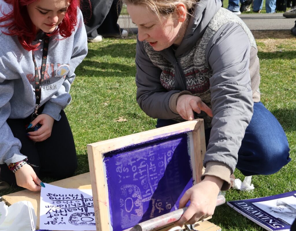 Claire Biesel (right) guides Quinnipiac University student Genevieve Brintall (left) as she creates her own print, offering the artwork for free. Hannah Freshman/HQNN