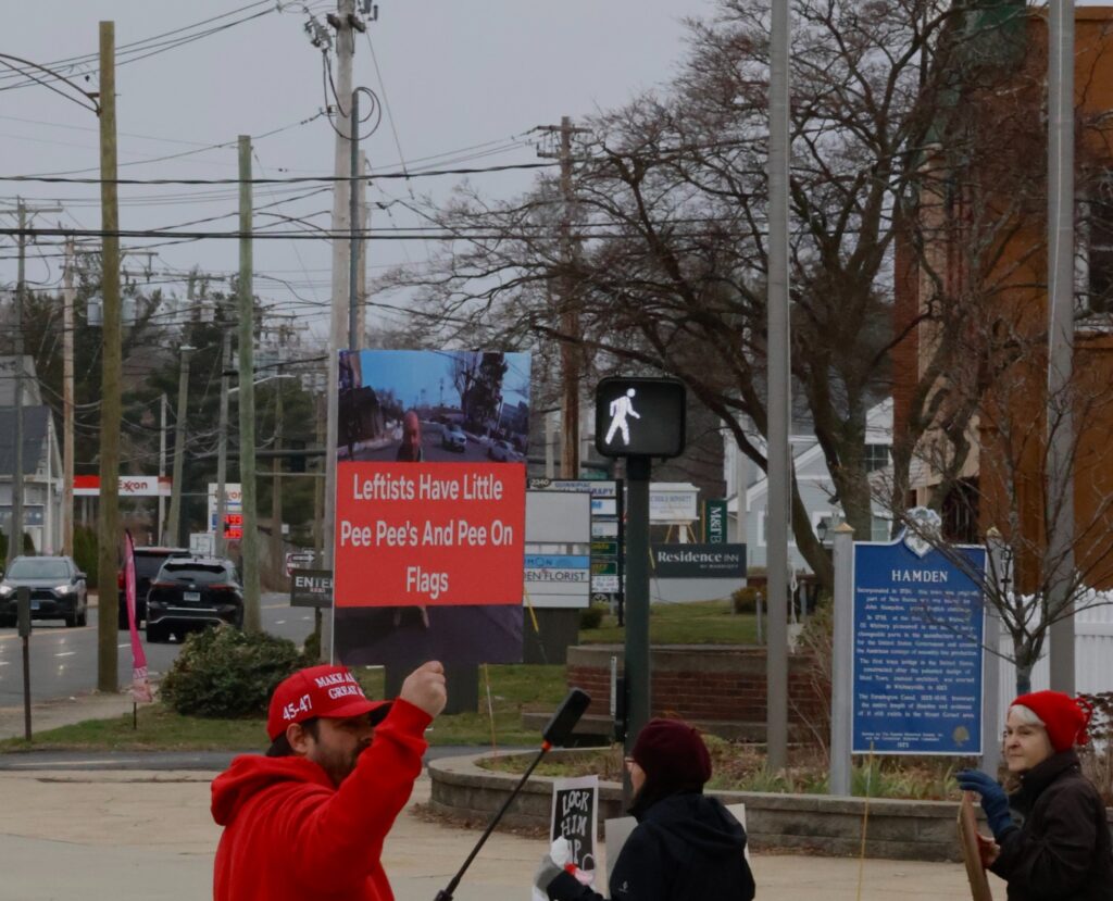 A sign held by counter-protester Robert Vardaro displays an explicit message as he stands with demonstrators. Protesters said Vardaro has repeatedly attempted to provoke confrontations during recent weekly rallies. Hannah Freshman/HQNN