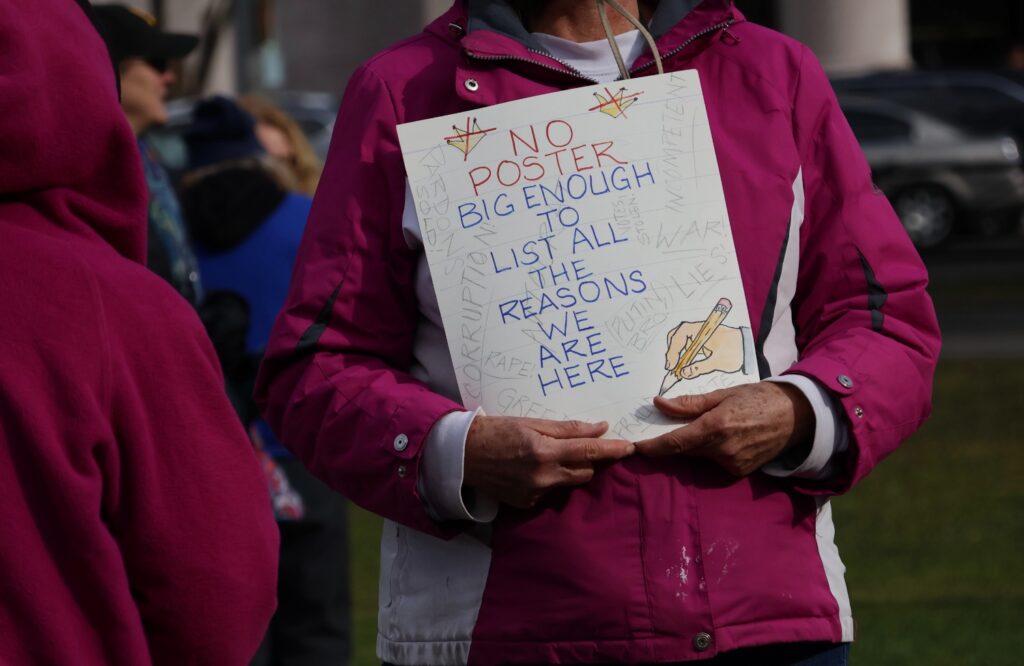 An unidentified protester holds a sign reading “No poster is big enough to list all of the reasons we are here” during the demonstration. Hannah Freshman/HQNN