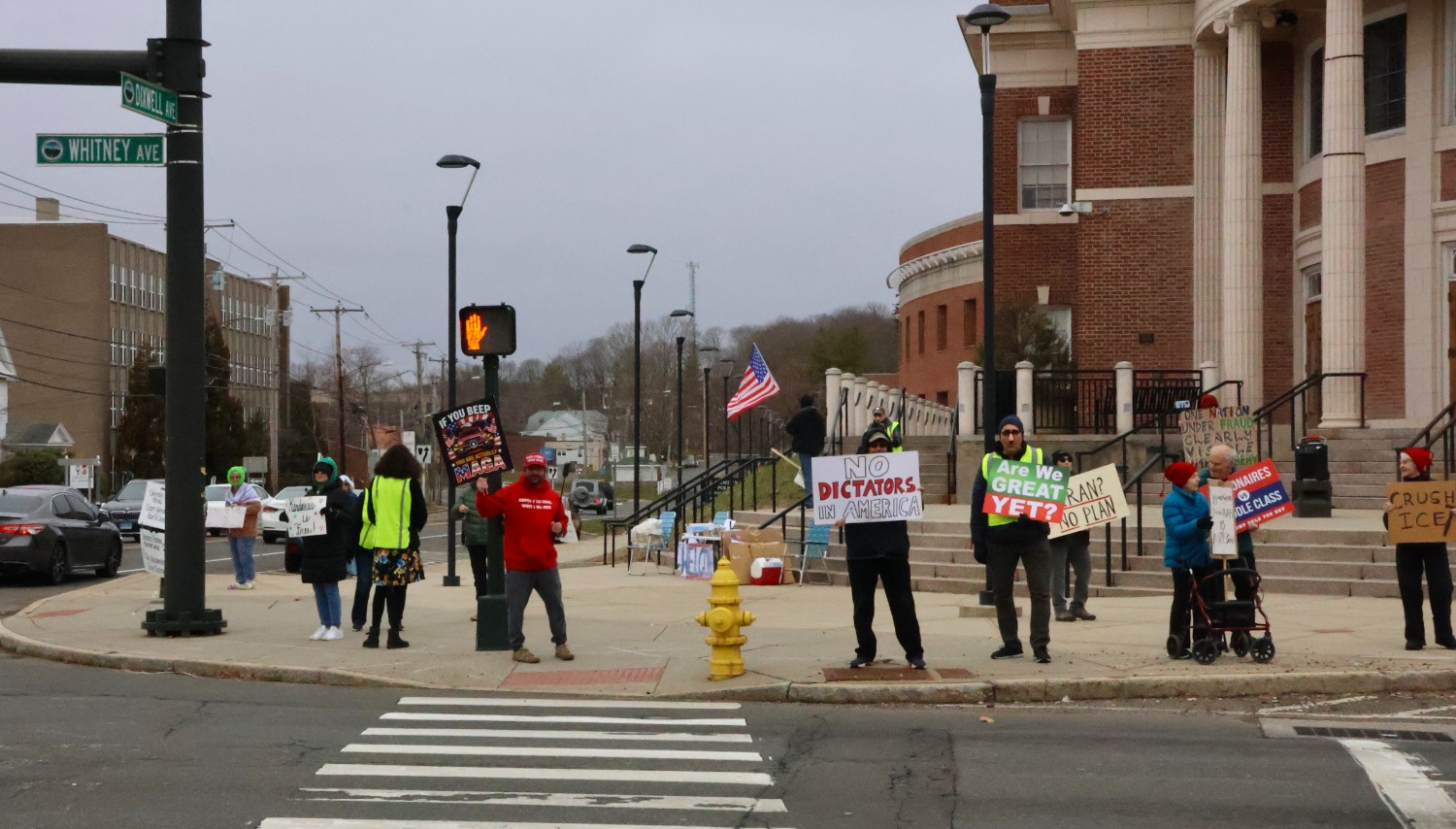 Seen from across the street, demonstrators gather as a counter-protester stands near the crosswalk in front of the group, highlighting ongoing tensions at the weekly rally. Hannah Freshman/HQNN
