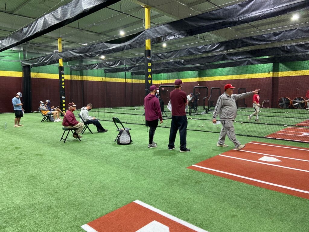 Ed DiPersio (right) walks past the batting cages at the D-BATS facility in Cheshire as two scouts from Springfield College watch a player taking batting practice. (photo by: David Rooney)