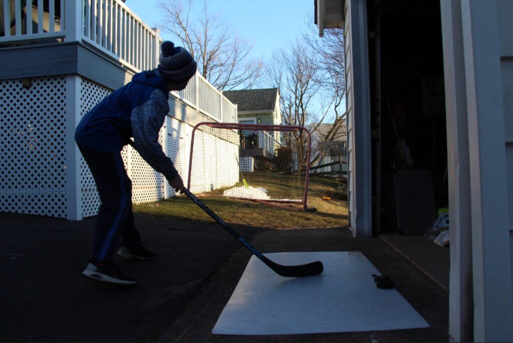Sean Studley, 13, loads back to shoot a puck into the net in his backyard. Photo Credit: Lo Yarnall